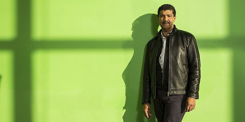 Pepón Osorio standing in front of a green wall. 