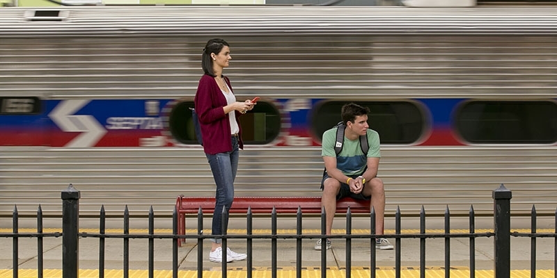 Two students waiting for a train at Temple University’s SEPTA Regional Rail Station as a train passes by. 