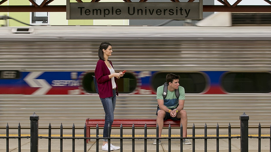 Two students waiting for a train at Temple University’s SEPTA Regional Rail Station as a train passes by. 