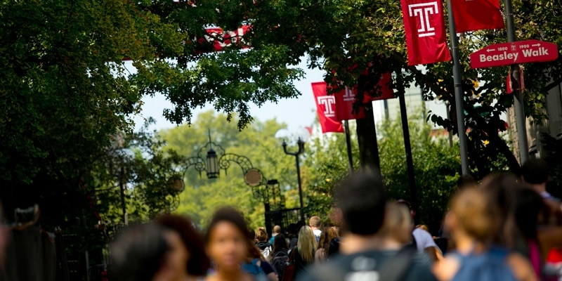 Students walking on campus under Temple ‘T’ flags.