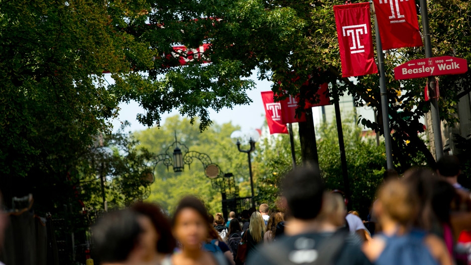 Students walking on campus under Temple ‘T’ flags.