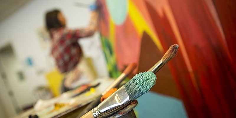 Paintbrushes and a woman painting in the background. 