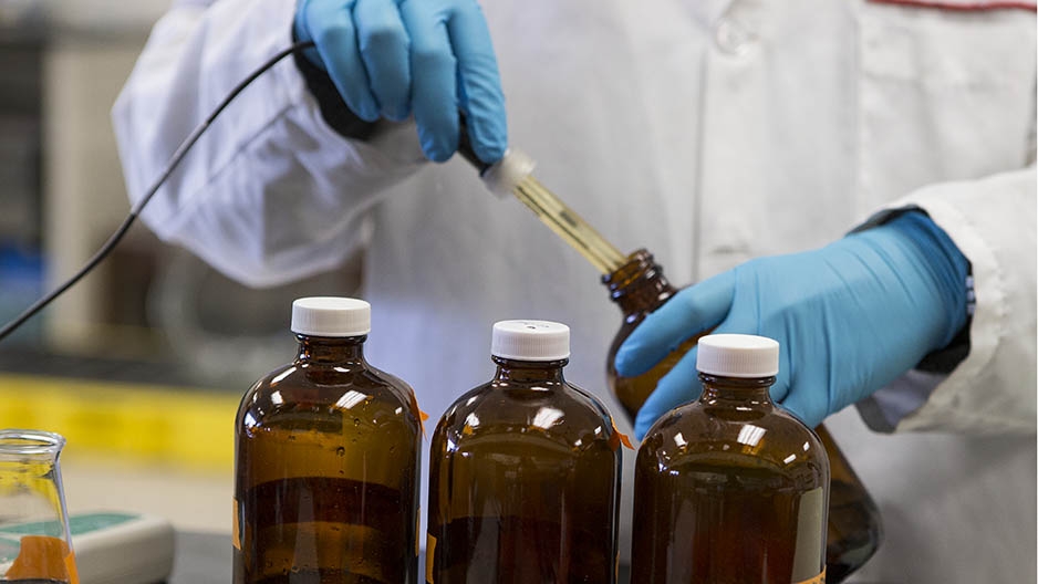 A scientist’s hand dropping liquid into test bottles.