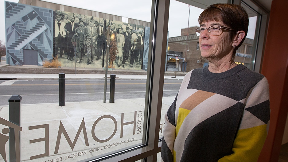 Sister Mary Scullion standing in front of a window, looking out on a mural. 
