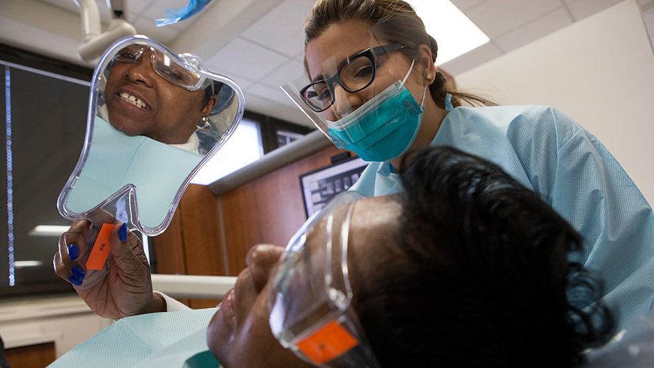 A female patient looking in a handheld mirror at her new dental crown.