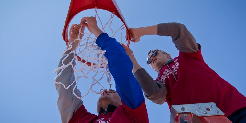 Two male student volunteers hanging a basketball net at Amos Recreation Center.  