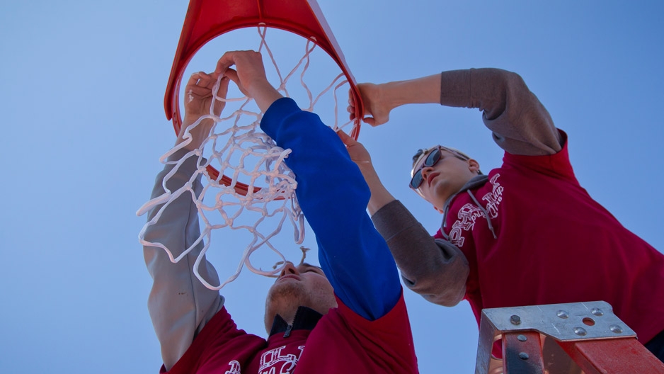 Two male student volunteers hanging a basketball net at Amos Recreation Center.  