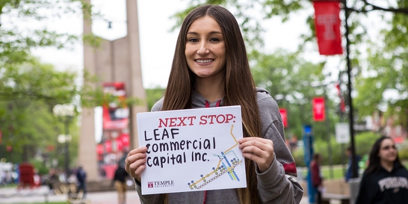 A woman with brown hair holding a sign that reads LEAF Commercial Capital, Inc.