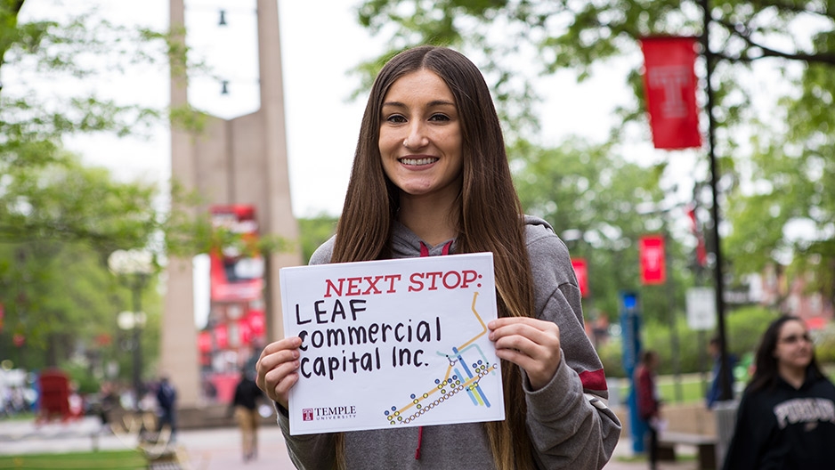 A woman with brown hair holding a sign that reads Leaf Commercial Capital, Inc.