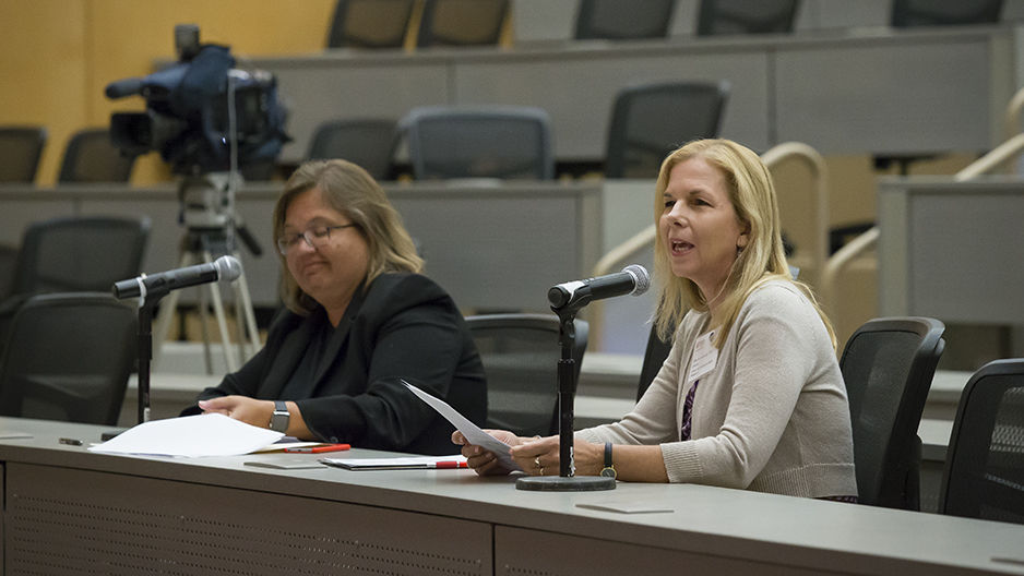 Two women sitting at a table and one is speaking into a microphone.