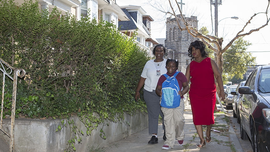 Two women and a young girl walking together through a residential neighborhood in North Philadelphia.