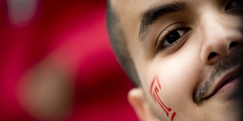 A close up of a man with a red Temple “T” painted on his face. 