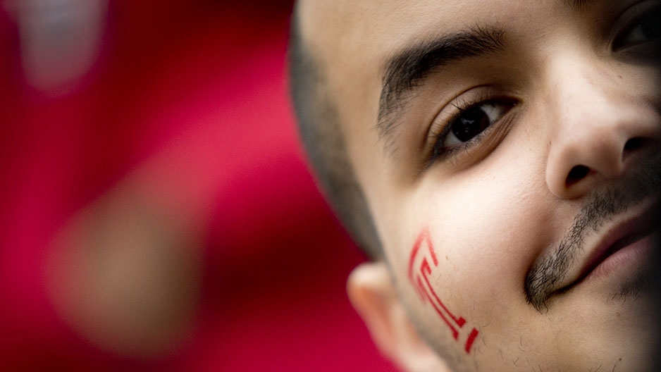 A close up of a man with a red Temple “T” painted on his face. 
