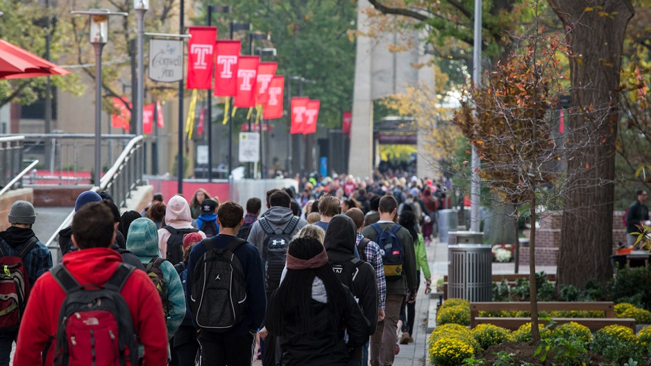 students walking on campus underneath red flags bearing the Temple ‘T’.