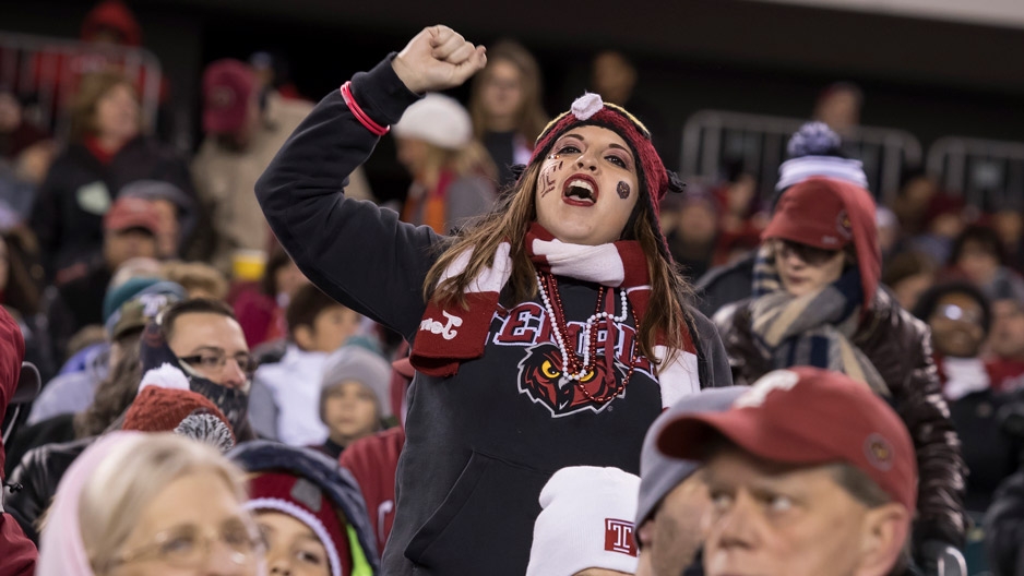 a fan in the crowd wearing Temple gear, cheering on the Temple football team.