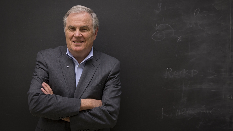 Thomas Edwards standing in front of a chalkboard with his arms crossed. 