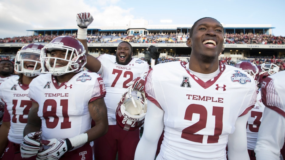 Temple football players smiling and celebrating on the field after a big win.