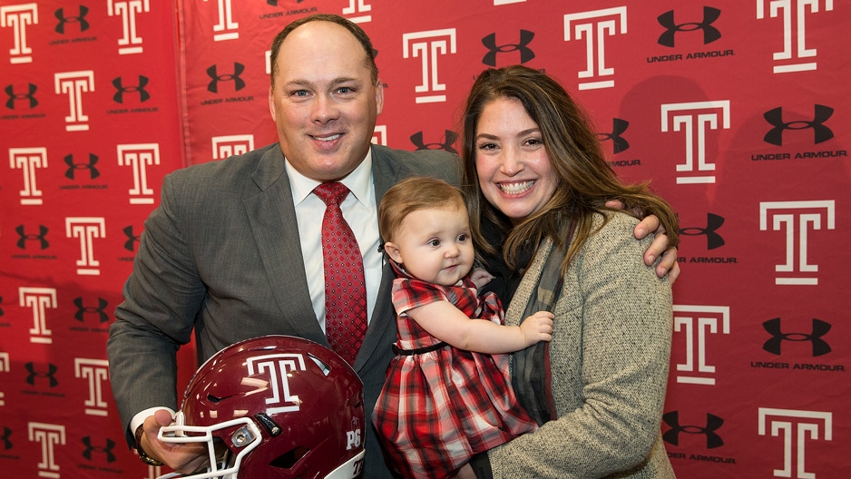 Geoff Collins holding a Temple helmet and smiling with wife and baby daughter.