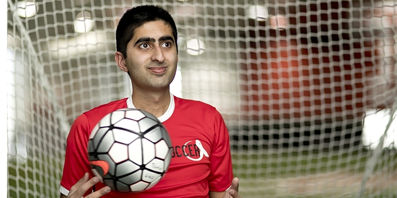 Haseeb Goheer holding a soccer ball in front of a goal net. 