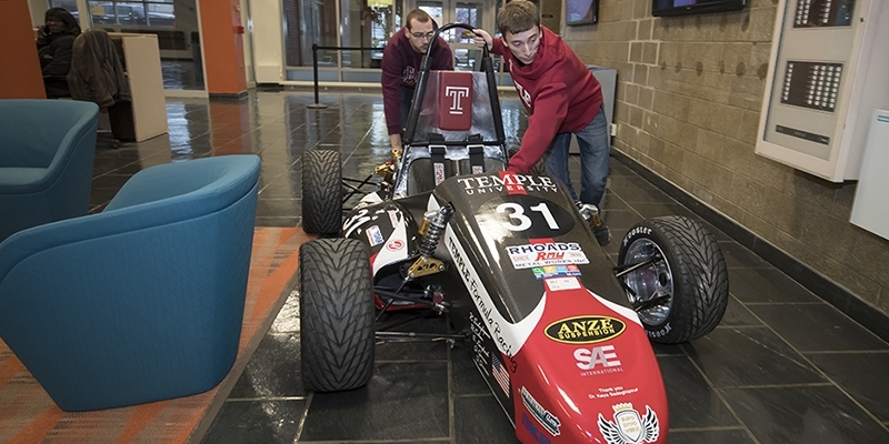 Two students pushing the race car through the engineering building. 