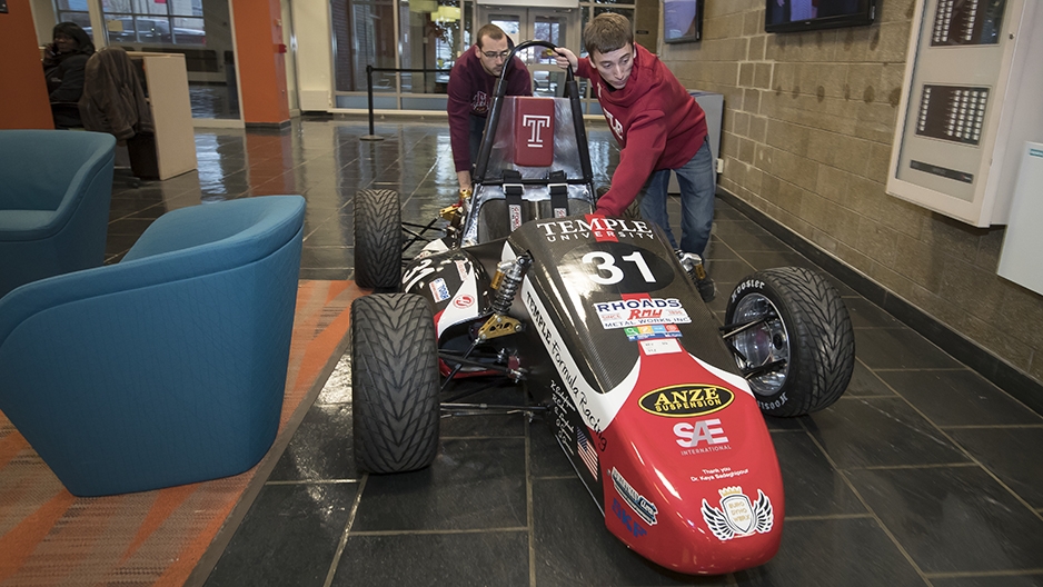 Two students pushing the race car through the engineering building. 