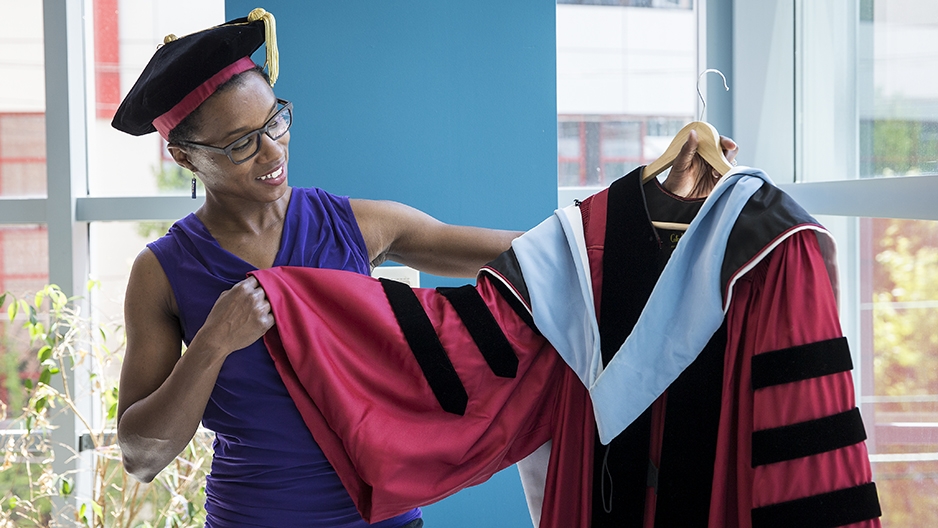 Musu Davis holding and eyeing the cherry graduation gown