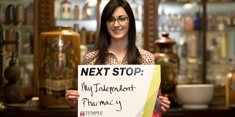 A woman holding a sign that reads next stop: my independent pharmacy.