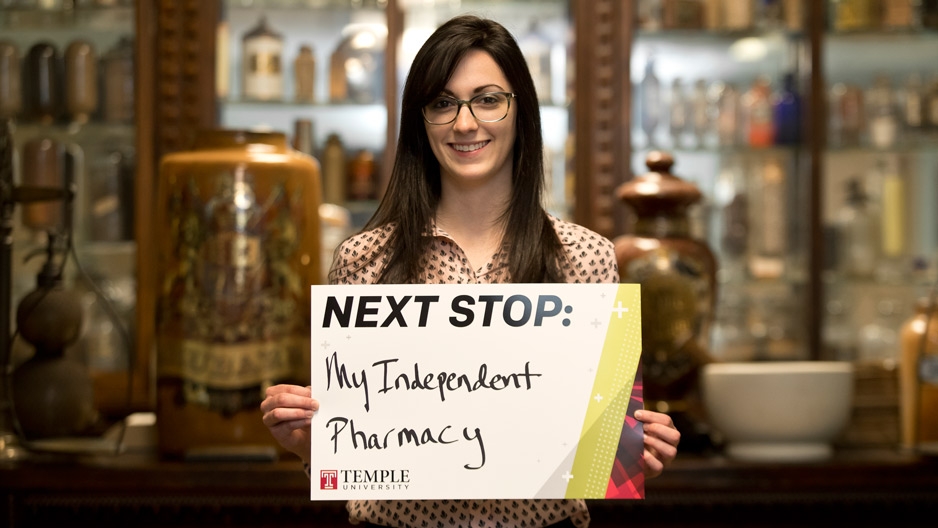 A woman holding a sign that reads next stop: my independent pharmacy.