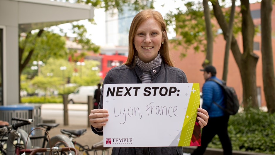 Amelia Schunder holding up a sign that says Next Stop: Lyon, France