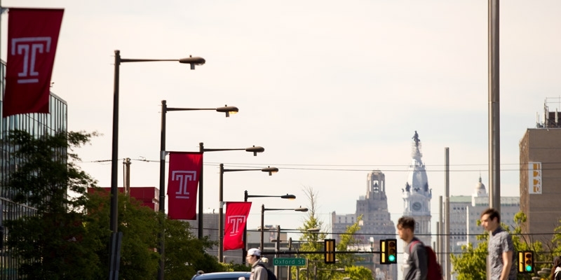 Students crossing Broad Street under red Temple flags.