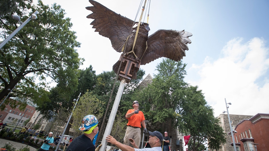 construction workers watch as a bronze owl statue is lowered