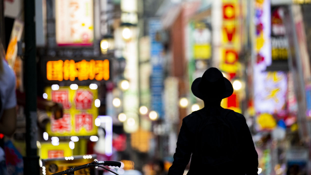A figure silhouetted against illuminated street signs in Tokyo.