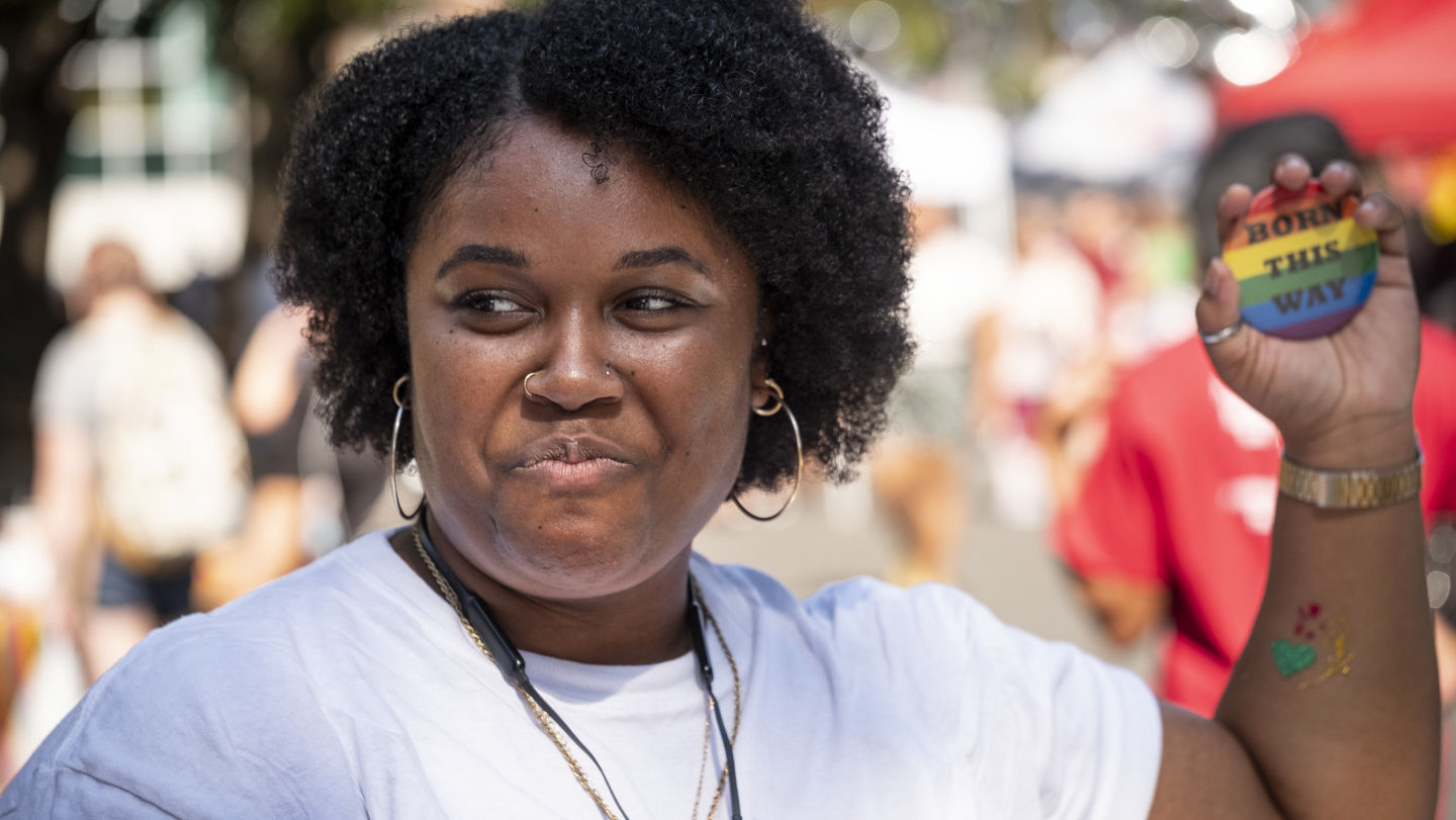 A Temple student holding up a rainbow colored pin that says "born this way." 