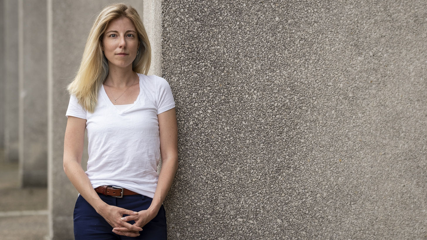 Jennifer Pollitt standing in front of a concrete building, wearing a white t-shirt.