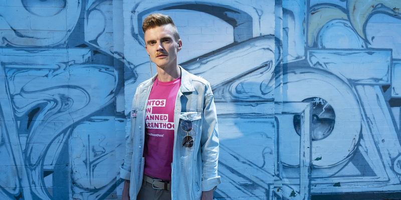 Andreas Copes in front of a blue background, wearing a Planned Parenthood shirt.