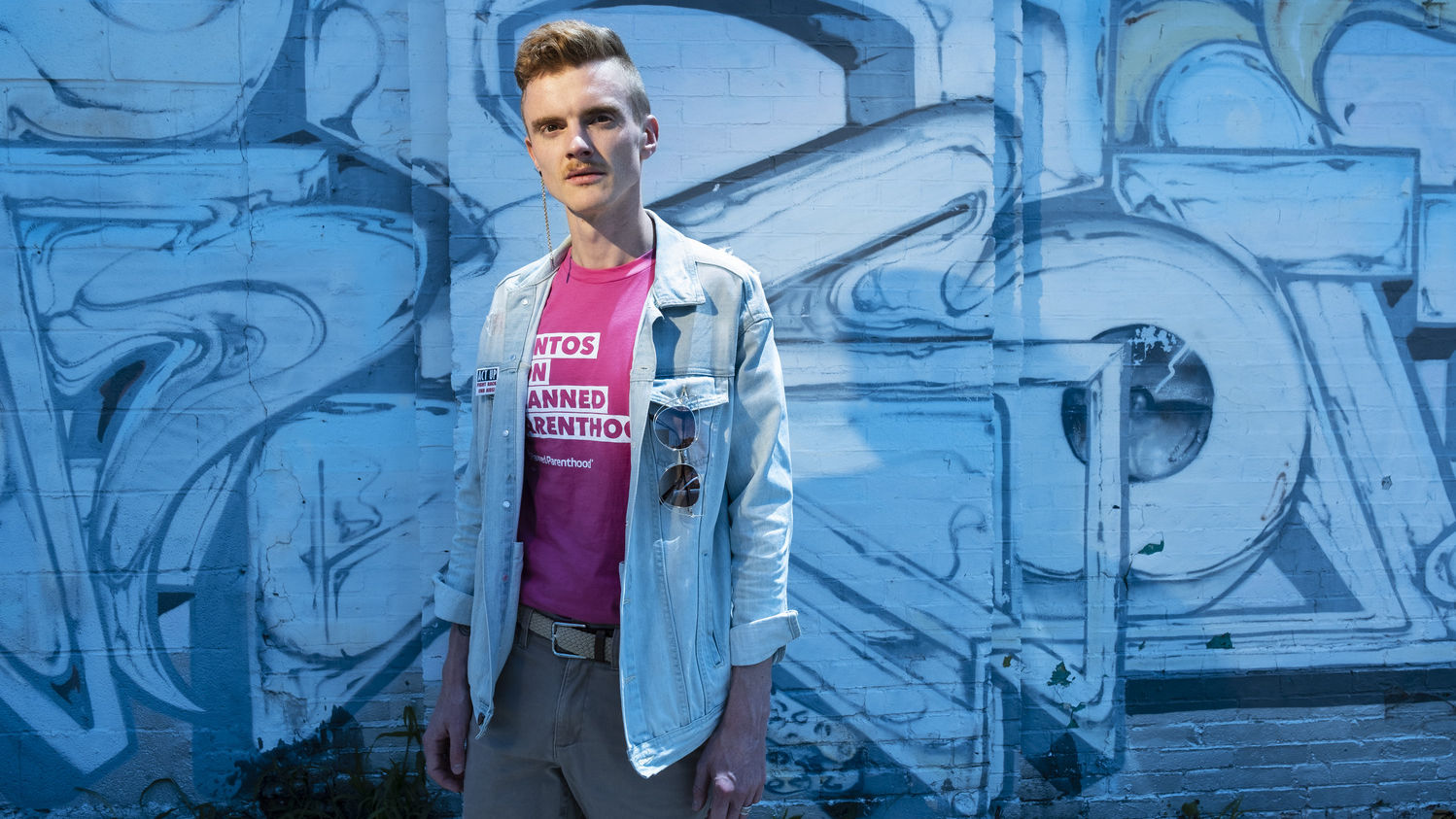 Andreas Copes in front of a blue background, wearing a Planned Parenthood shirt.