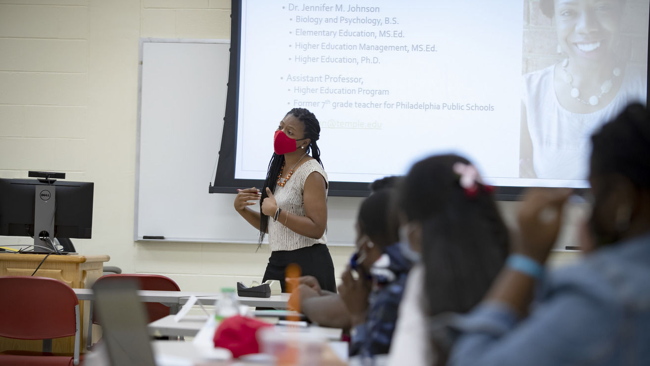 A woman in a red face covering standing before an overhead projector screen.