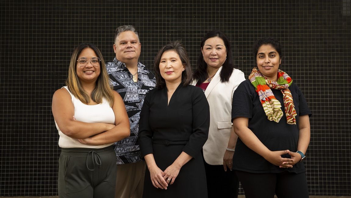 A group of Temple staff members standing in front of a black tiled wall. 