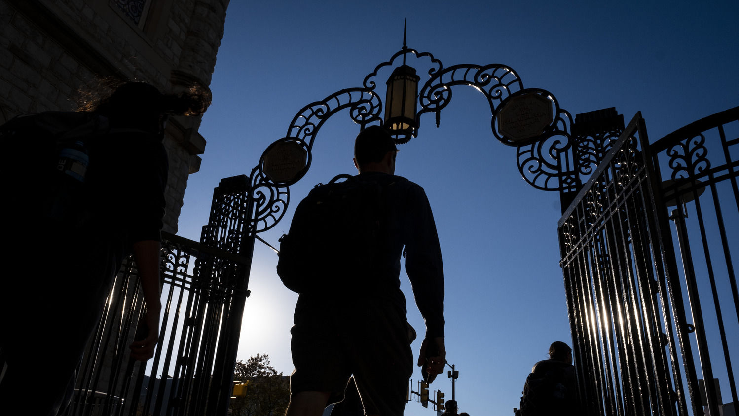A student in silhouette walks through gates on Temple's Main Campus.