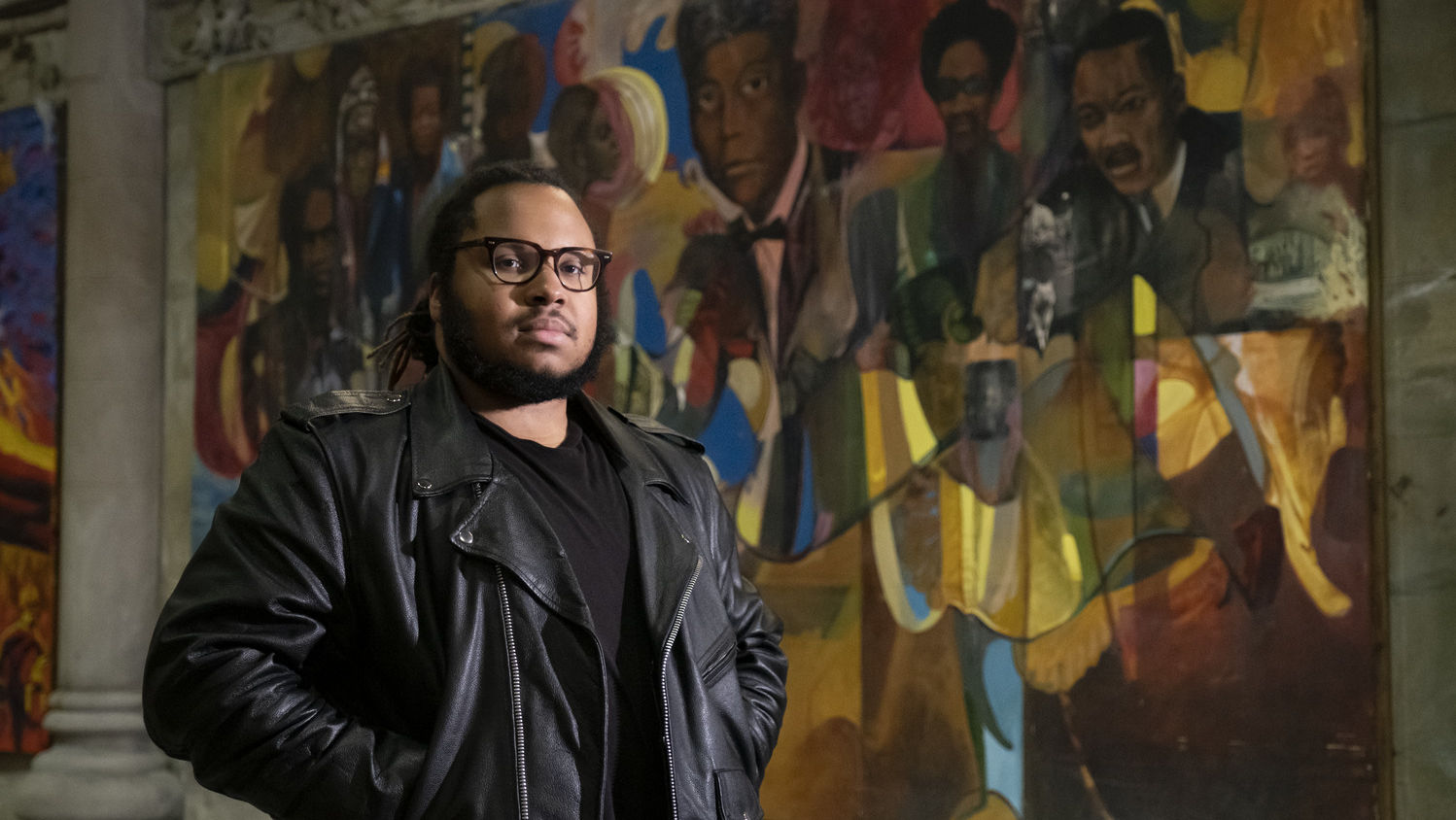 Tyler A. Ray stands in front of one of 14 murals inside the Church of the Advocate.
