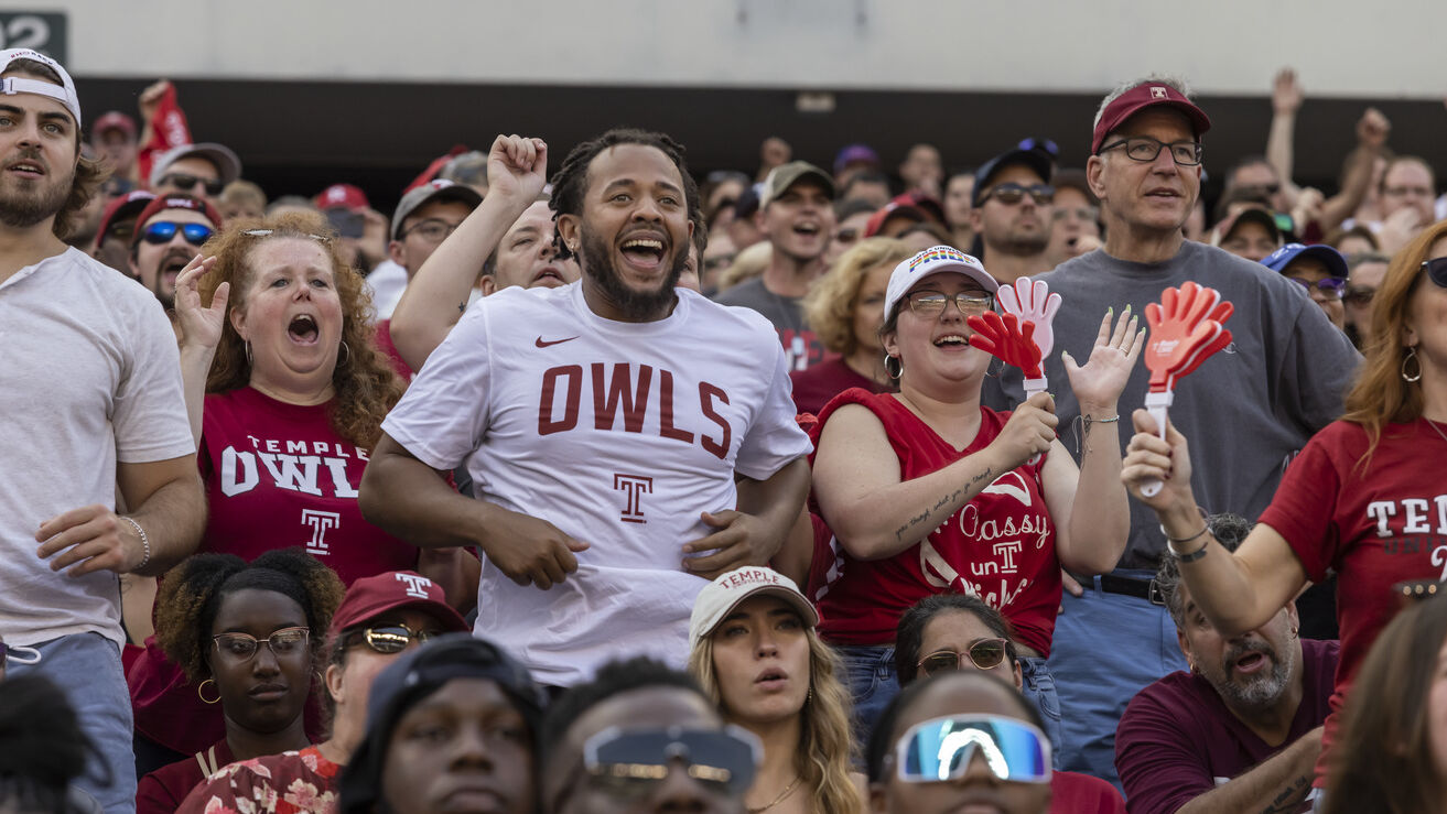 Image of a smiling college football fans wearing Temple-branded shirts.  