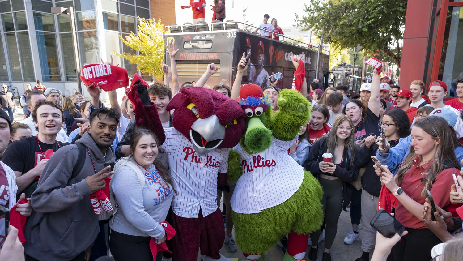 A group of smiling Temple students wearing red shirts and waving Red October towels celebrate the Philadelphia Phillies.