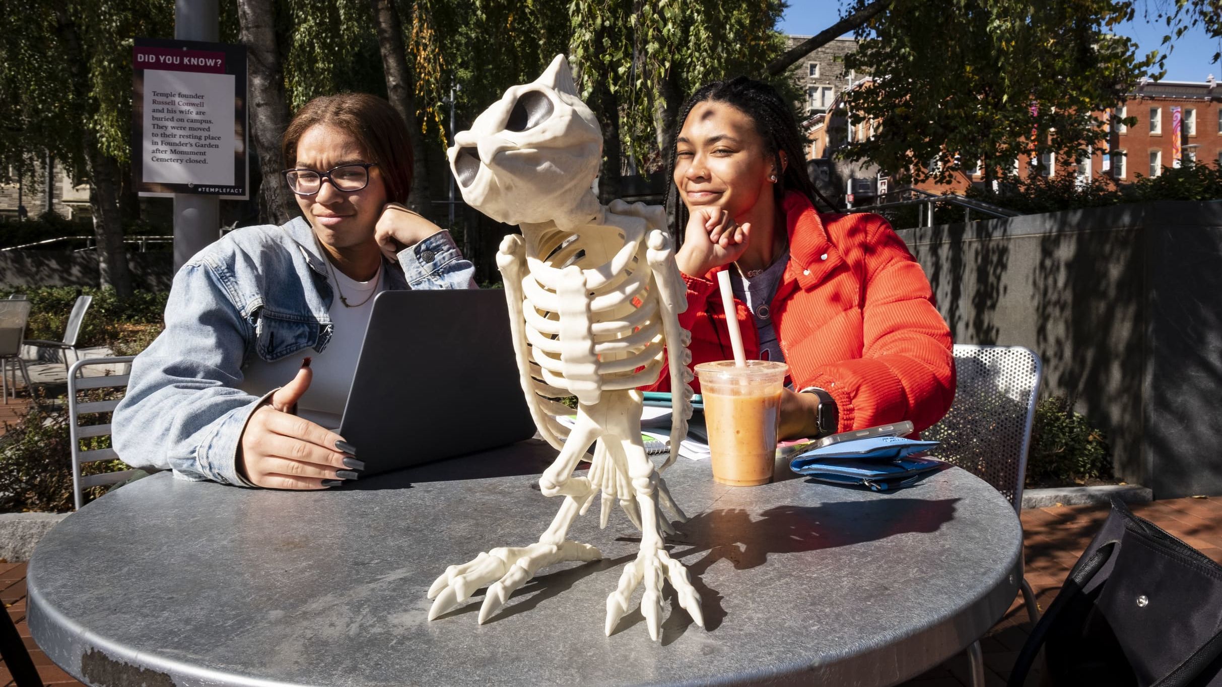 Two students sitting at a table outside with a skeleton