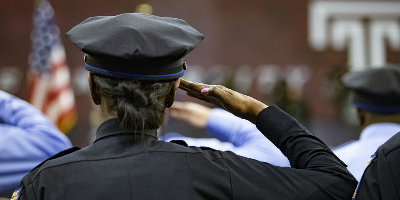 Newly sworn-in police officer salutes the American flag with Temple logo behind it.