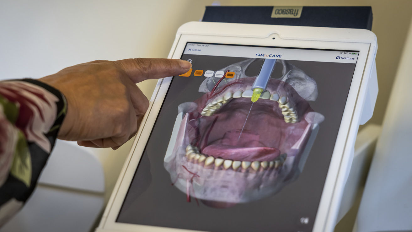 A finger points at a digital model of a mouth on a screen