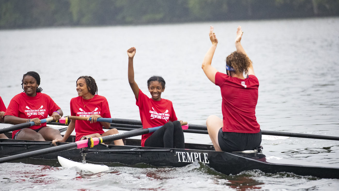 Image of children with smiles wearing red t-shirts, rowing a boat.  