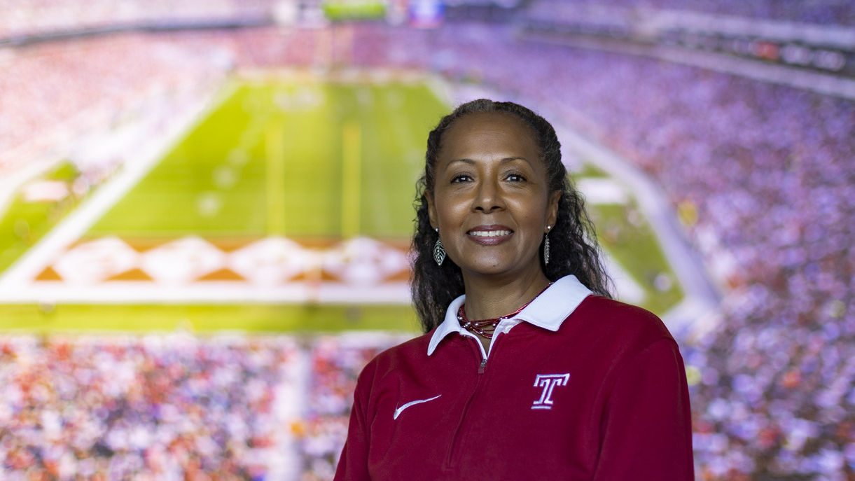 A woman wearing a cherry and white Temple shirt pictured with the background of Lincoln Financial Field. 