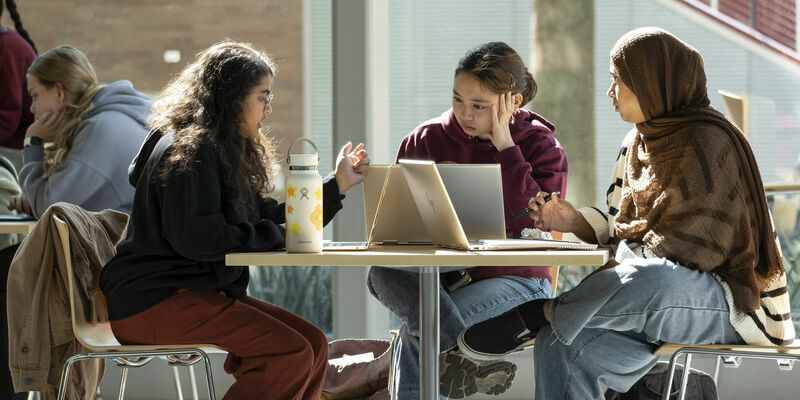Three students at a table working on laptops