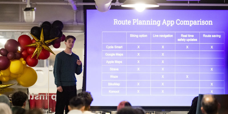 Image of a student speaking on stage in front of presentation  