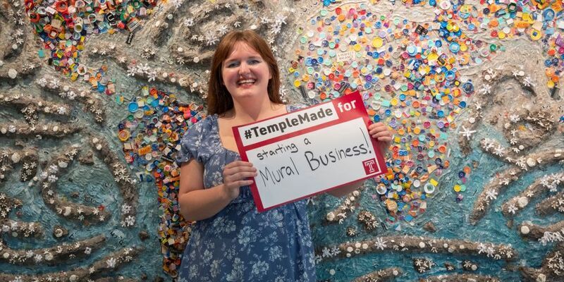 Abigail McNavage holding a #TempleMade sign in front of her painting 
